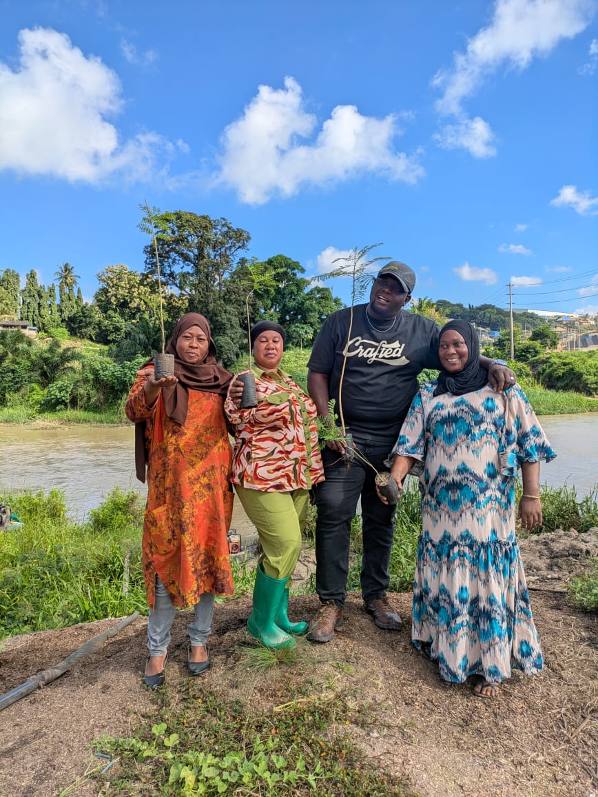 Community members holding tree saplings by a riverside