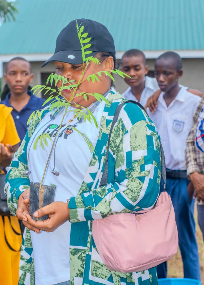 Student in a Green Rise jacket holding a tree seedling at school